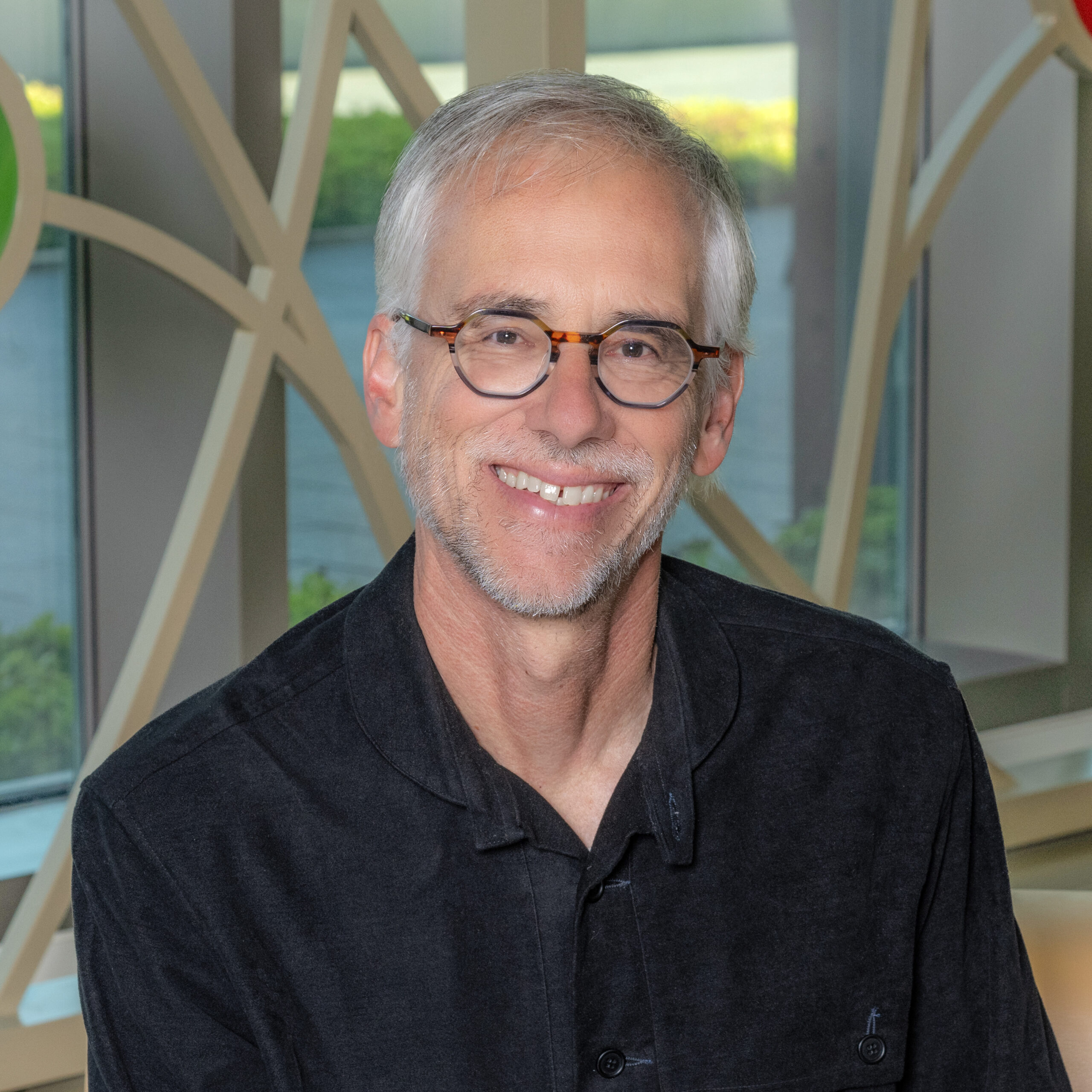 A white man with gray hair, glasses, and a close-cropped beard wearing a black shirt smiling.