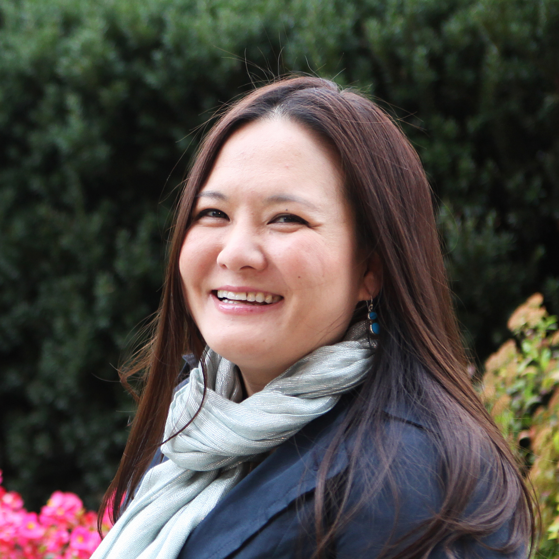 Asian woman with shoulder-length brown hair, blue neck scarf and jacket, smiling.